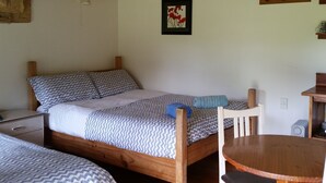 A bedroom with a wooden bed, a small table, and a chair. There is a framed picture on the wall and a shelf with a kettle. - Opua Garden Cottage, sleeps 3 (Collingwood)