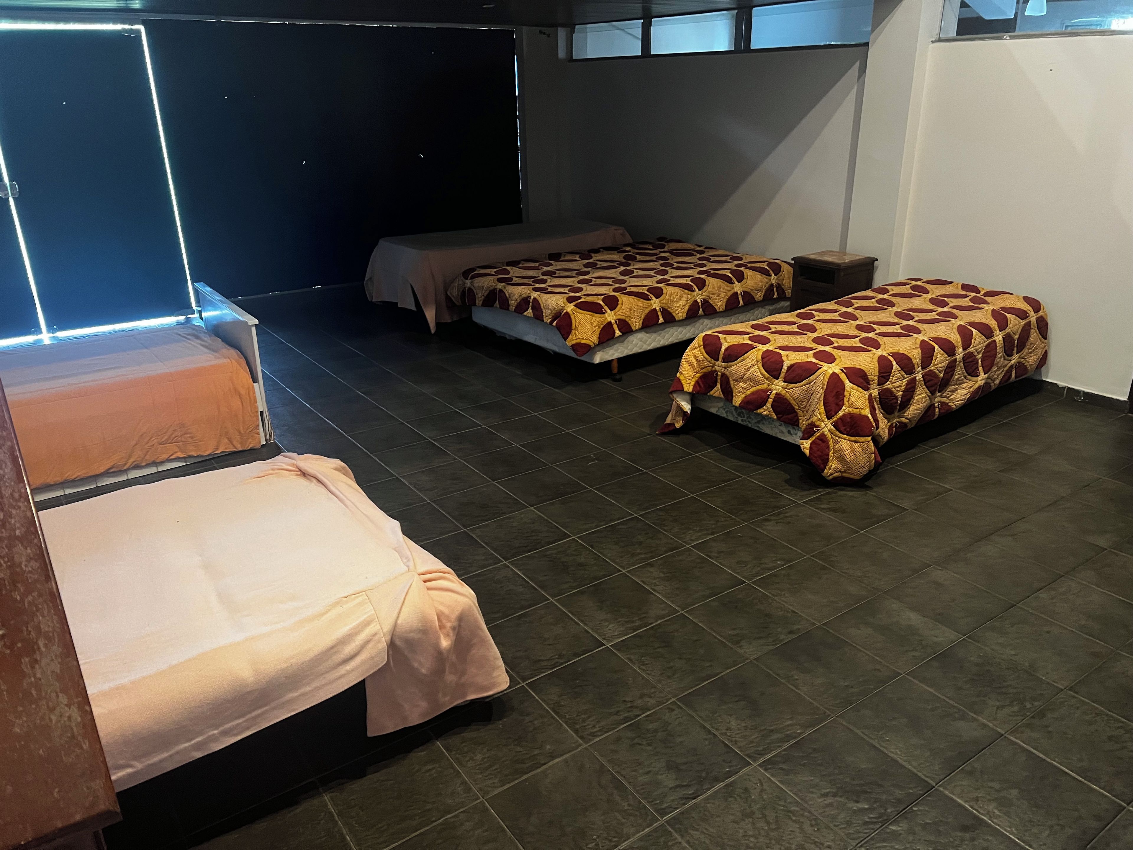 Une chambre avec trois lits, une petite table et une fenêtre.