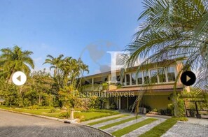 A two-story building with a balcony, surrounded by palm trees and a well-maintained lawn. - Stunning house on Pernambuco Beach - Guarujá (Balneario Praia do Pernambuco)