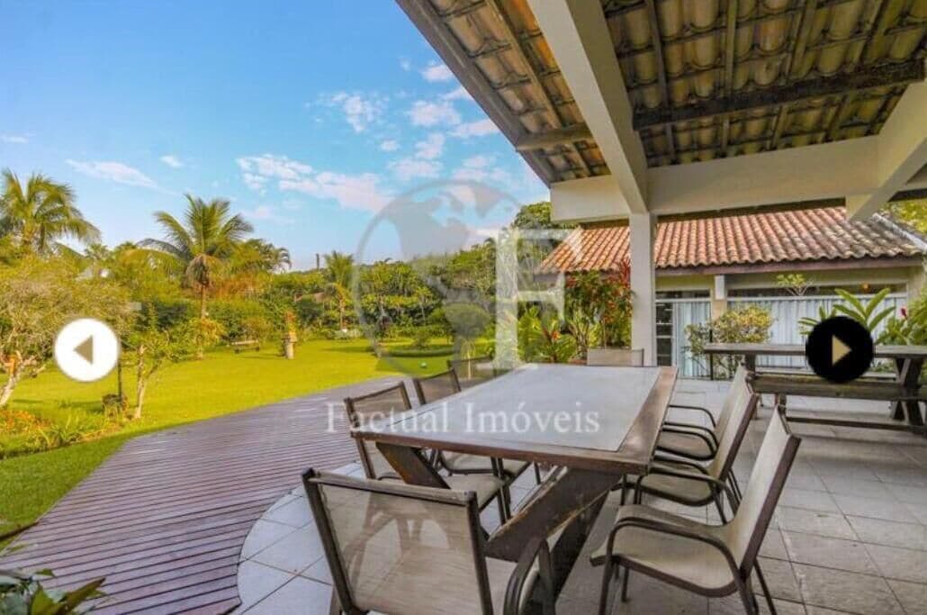 An outdoor patio area with a table and chairs, surrounded by greenery and a clear sky.