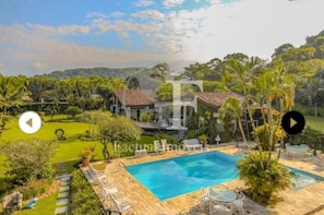 A residential property with a swimming pool, surrounded by lush greenery and a view of hills.