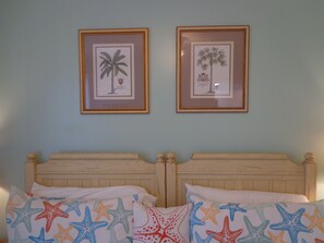 Quarto com cama de madeira, duas gravuras botânicas emolduradas na parede e almofadas com padrão de estrelas.