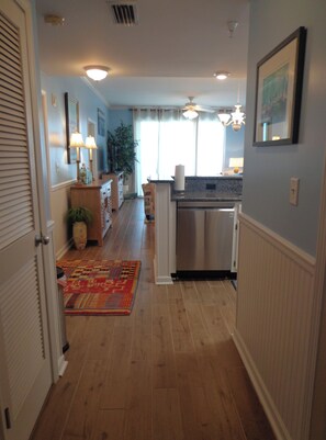 A narrow hallway with wooden flooring, a patterned rug, and a kitchen area with a dishwasher and cabinets. - Inn at Dauphin Island 304 Walk-In Shower, Updated with Wonderful Views!! (Dauphin Island)