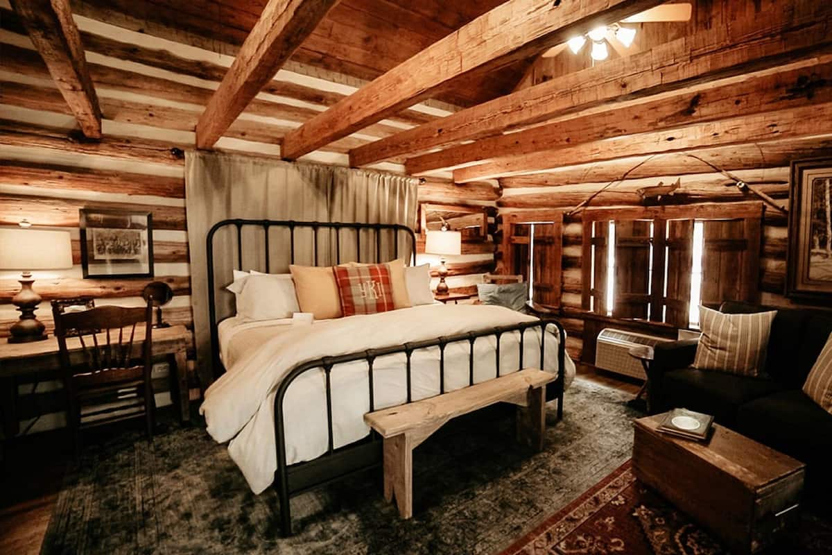 A rustic log cabin bedroom with a bed, a wooden bench, a sofa, and a small table.
