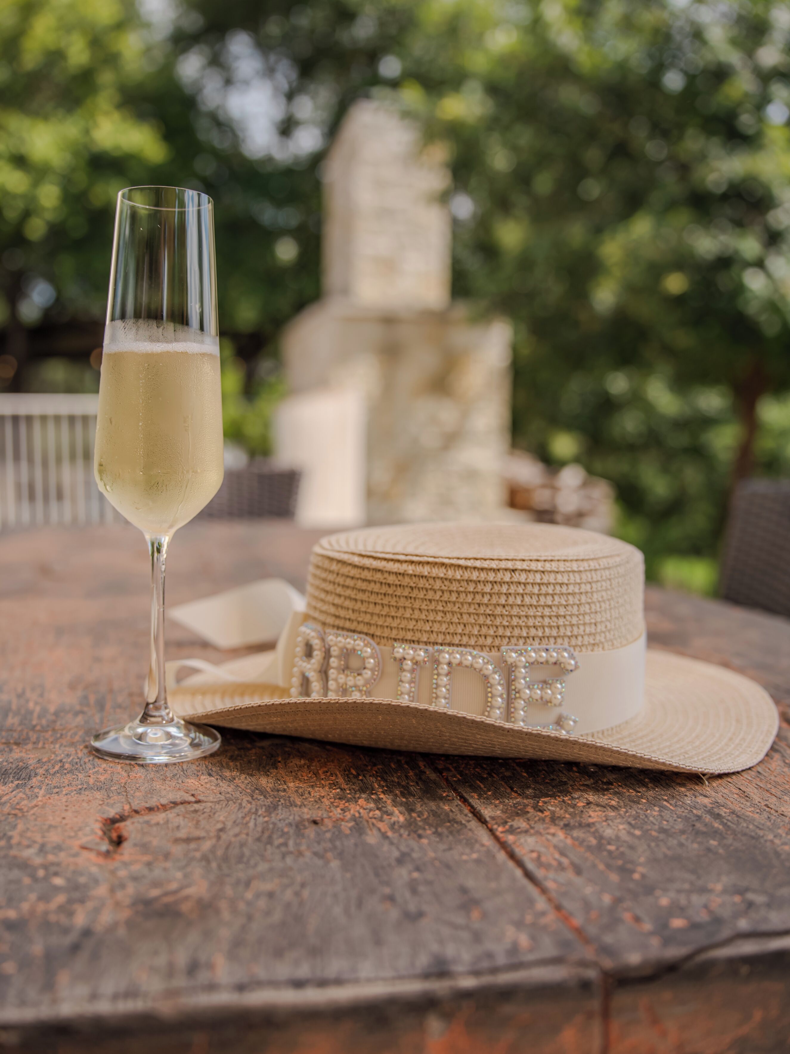 A glass of champagne, a straw hat, and a stone structure in the background.
