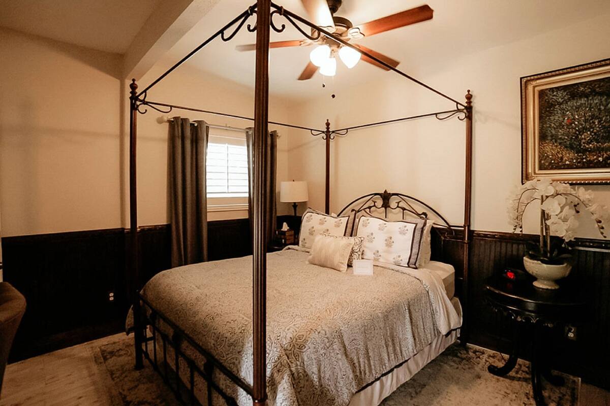A four-poster bed with a canopy, a nightstand with a lamp, and a framed picture on the wall.