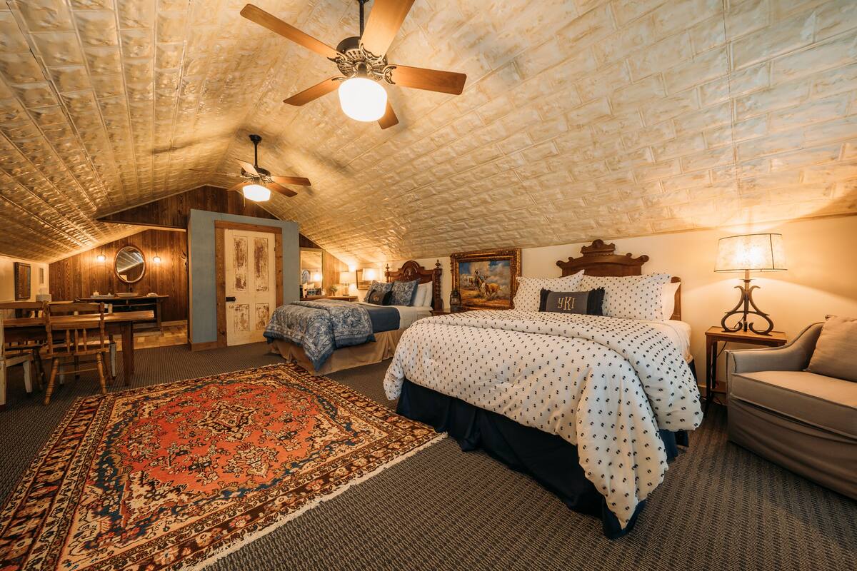 A spacious attic bedroom with a large bed, two smaller beds, a dining area, and a ceiling fan.