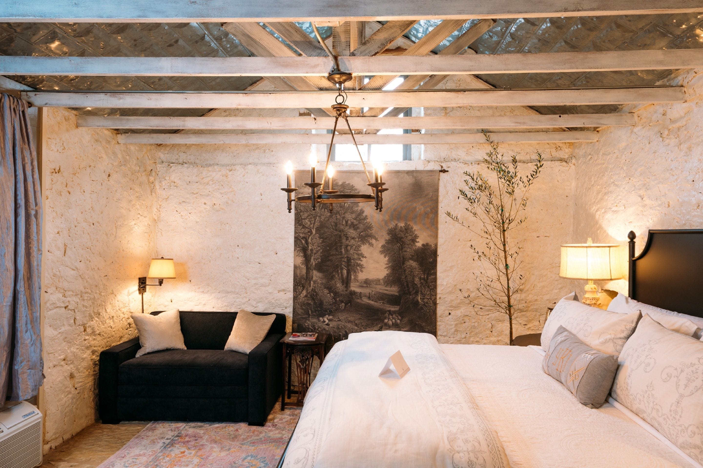 A bedroom with a bed, a sofa, a nightstand, a lamp, and a wall tapestry.