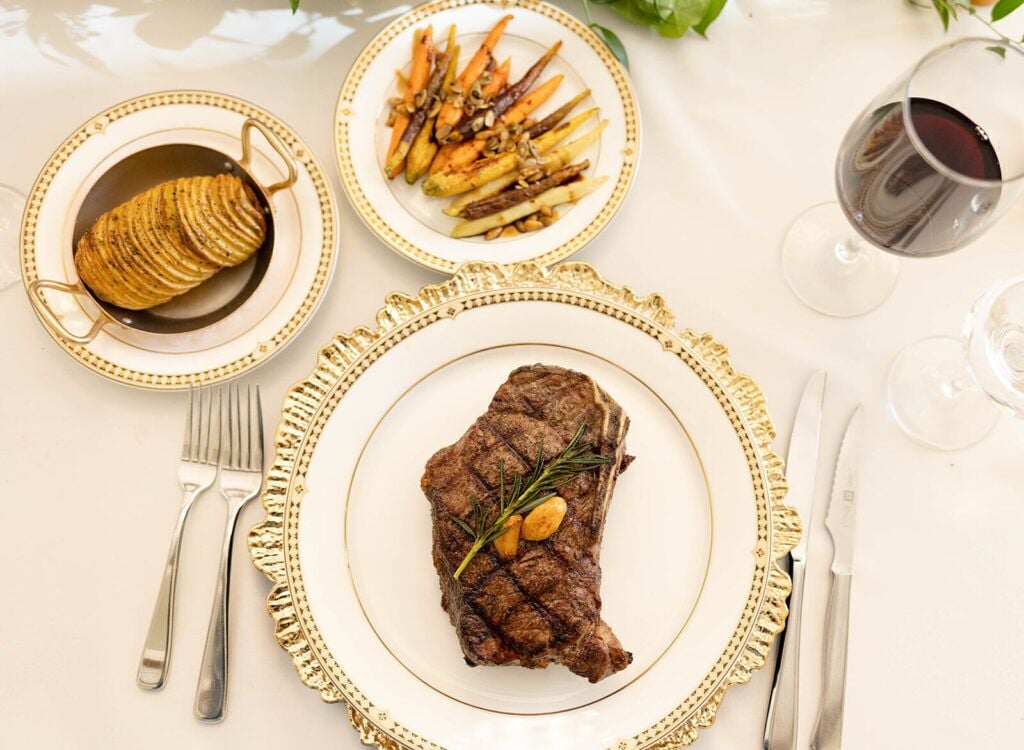 A neatly arranged dining table with a steak, roasted potatoes, and a glass of red wine.