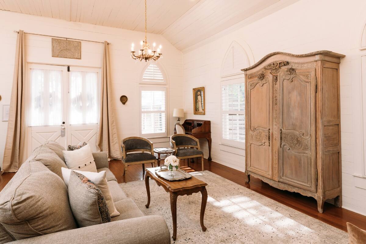 A cozy living room with a sofa, chairs, a wooden cabinet, and a chandelier.