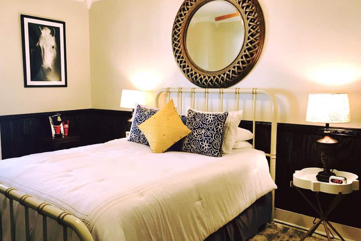 A neatly made bed with patterned pillows, a bedside table with a lamp, and a wall-mounted mirror.