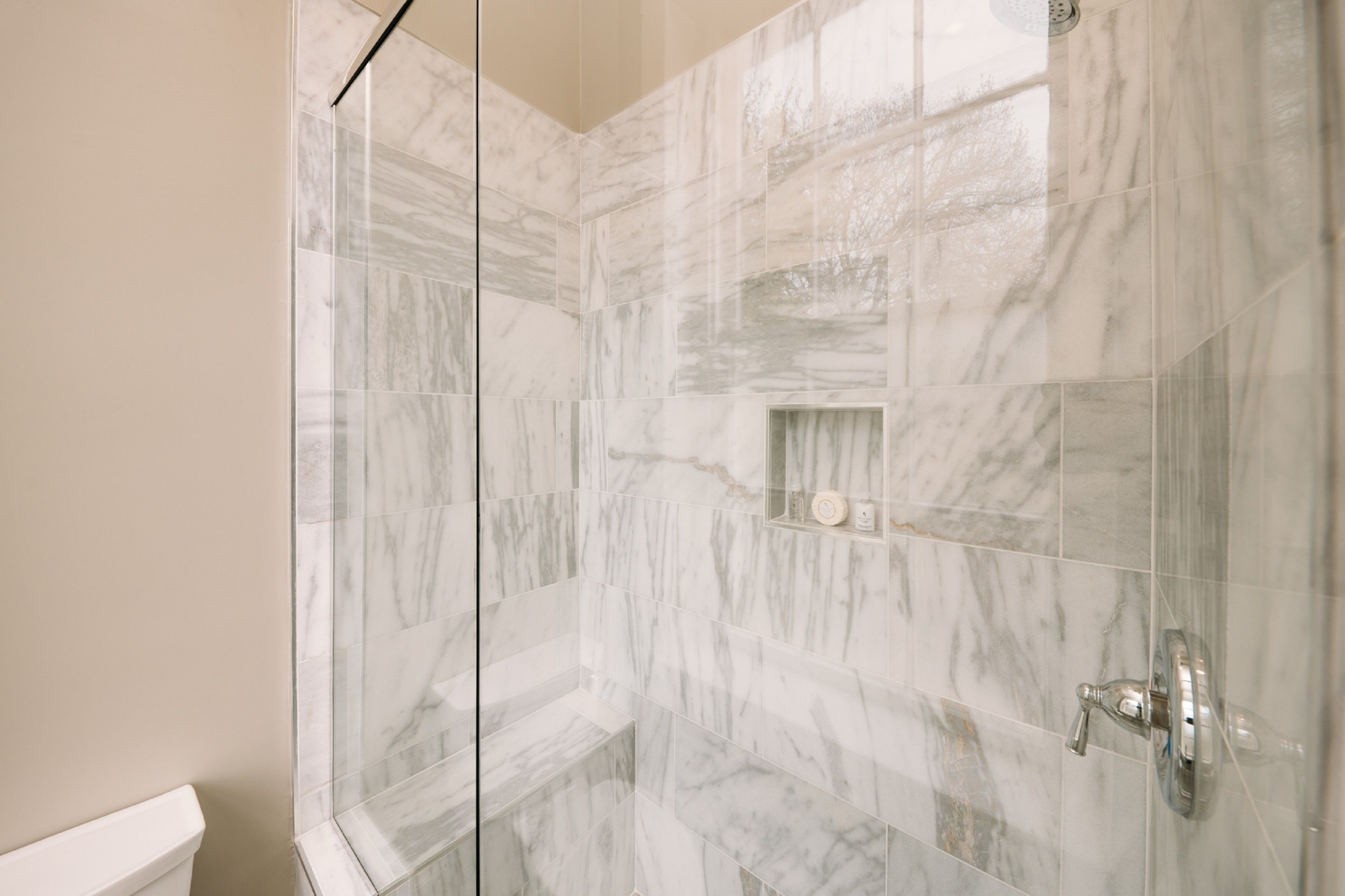 A bathroom with marble tiles, a glass shower enclosure, and a toilet.