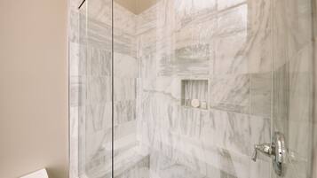 A bathroom with marble tiles, a glass shower enclosure, and a toilet.