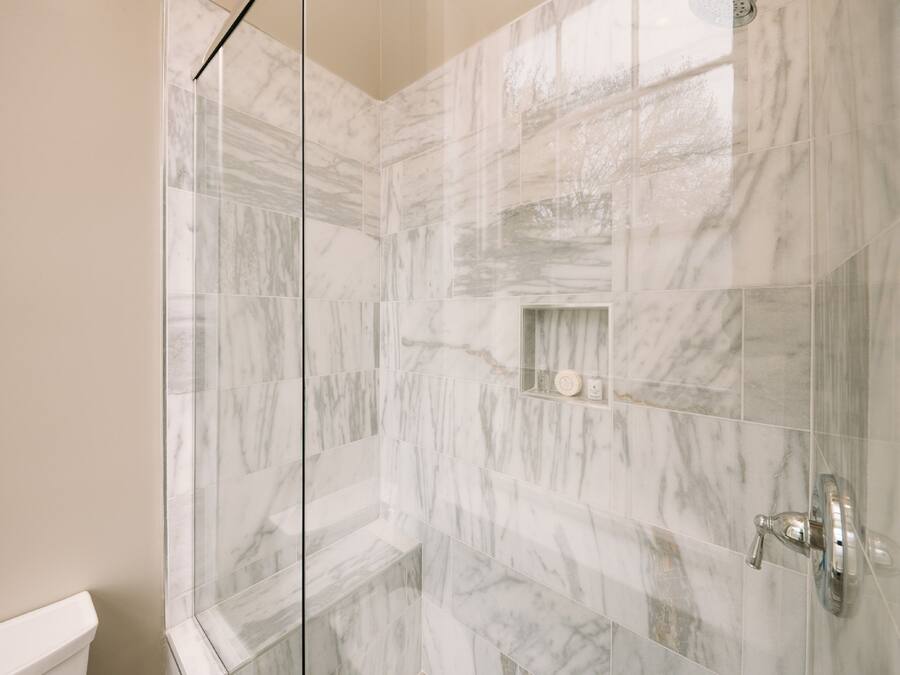 A bathroom with marble tiles, a glass shower enclosure, and a toilet.