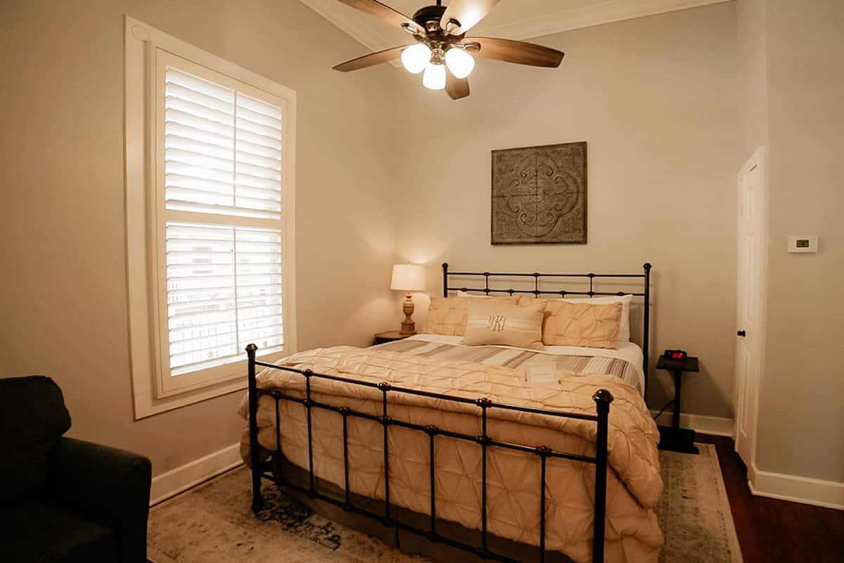 A bedroom with a bed, a ceiling fan, a window with blinds, a nightstand, and a door.