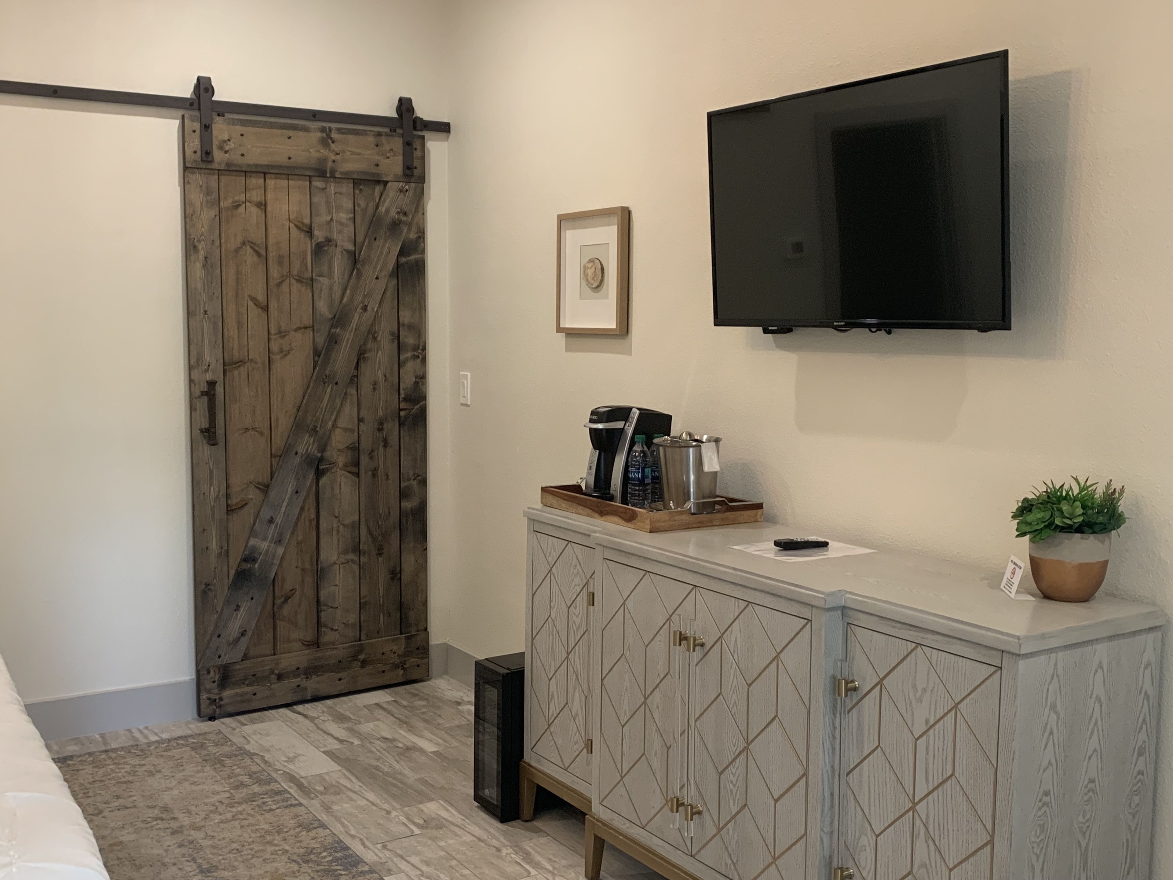 A bathroom with a wooden sliding door, a mounted TV, a cabinet with drawers, a sink, and a small potted plant.