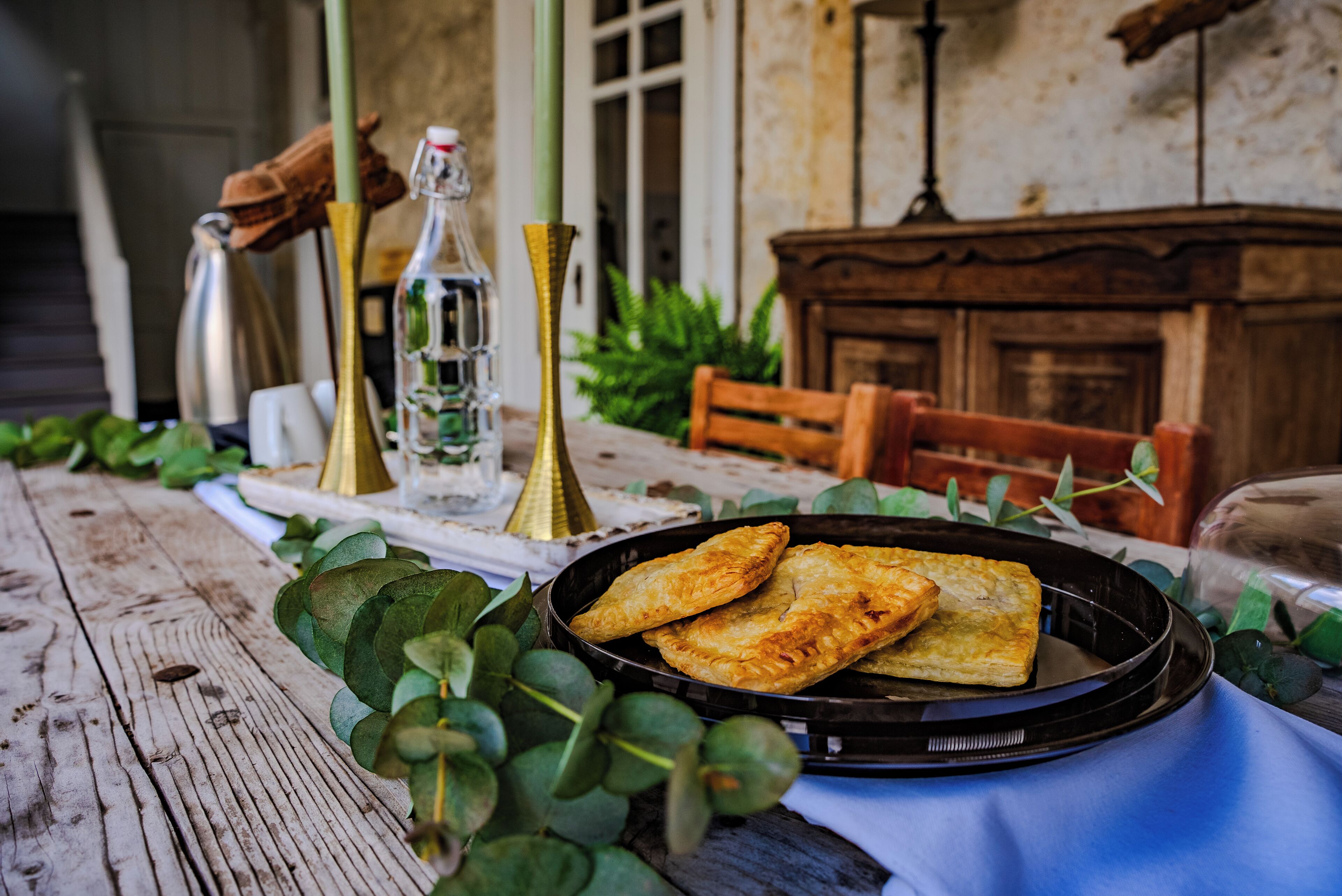 A rustic wooden table with a black plate holding pastries, surrounded by greenery and vintage-style decor.