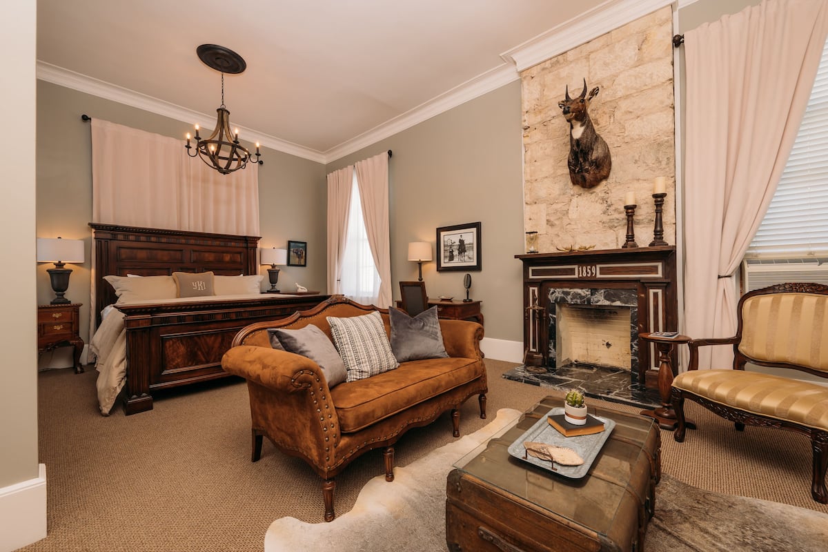 A traditional room with a bed, a sofa, a fireplace, and a chandelier.