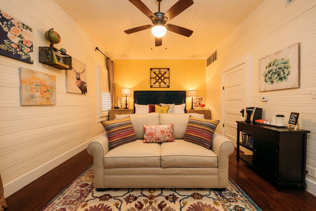 A cozy living room with a beige sofa, patterned rug, and a ceiling fan.