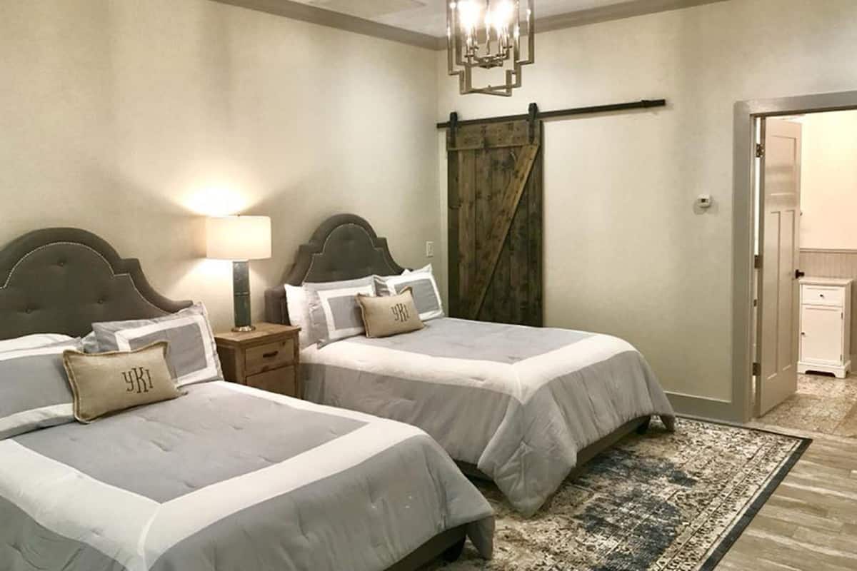 A bedroom with two beds, a nightstand, a lamp, a chandelier, a sliding barn door, and a rug.