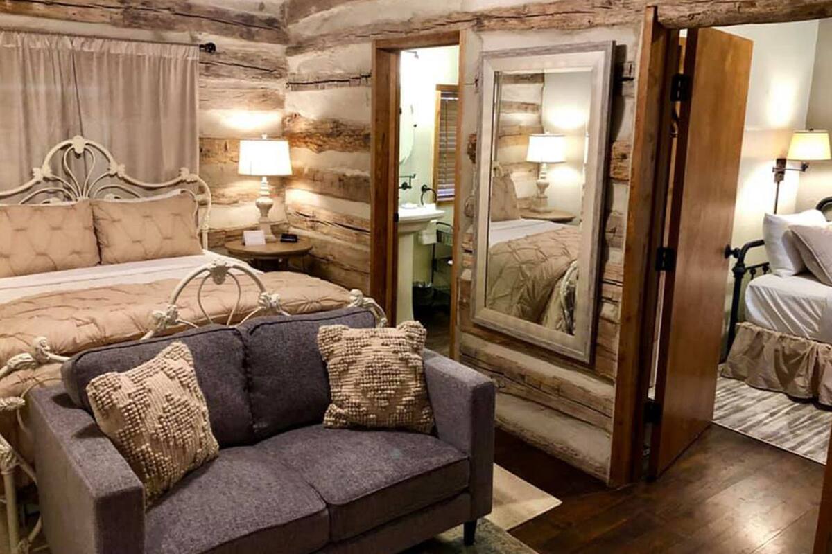 A rustic bedroom with a large bed, a sofa, a mirror, and a wooden door.