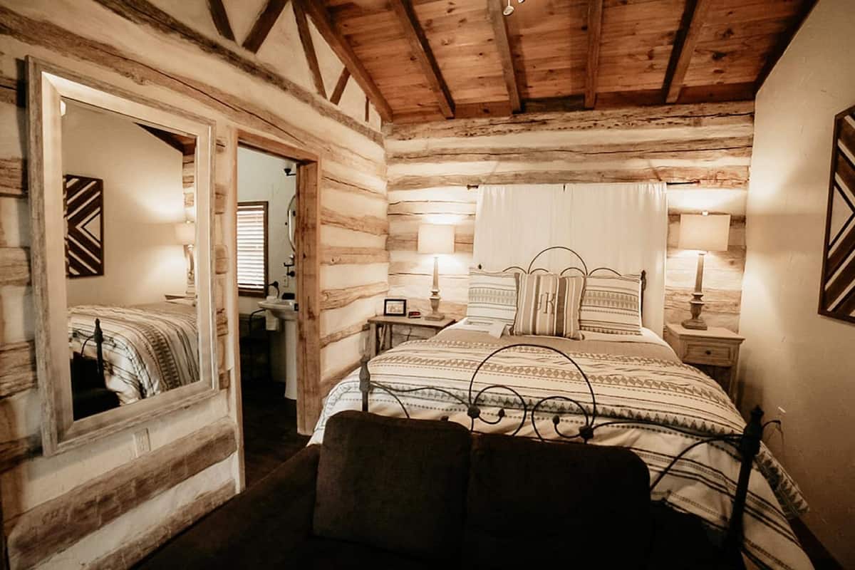 A log cabin bedroom with a large bed, two bedside tables, and a mirror.
