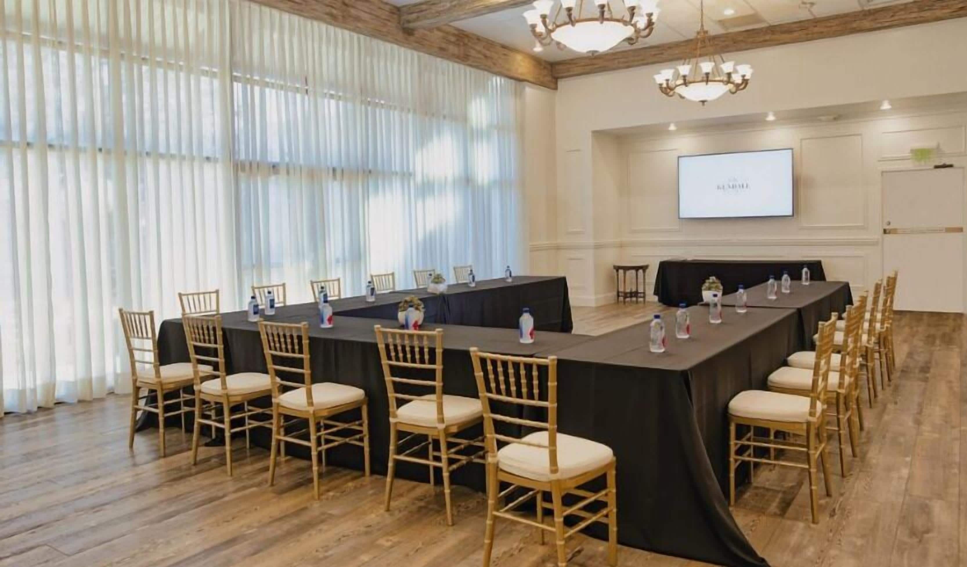A conference room with a long table, chairs, a projector screen, and a chandelier.