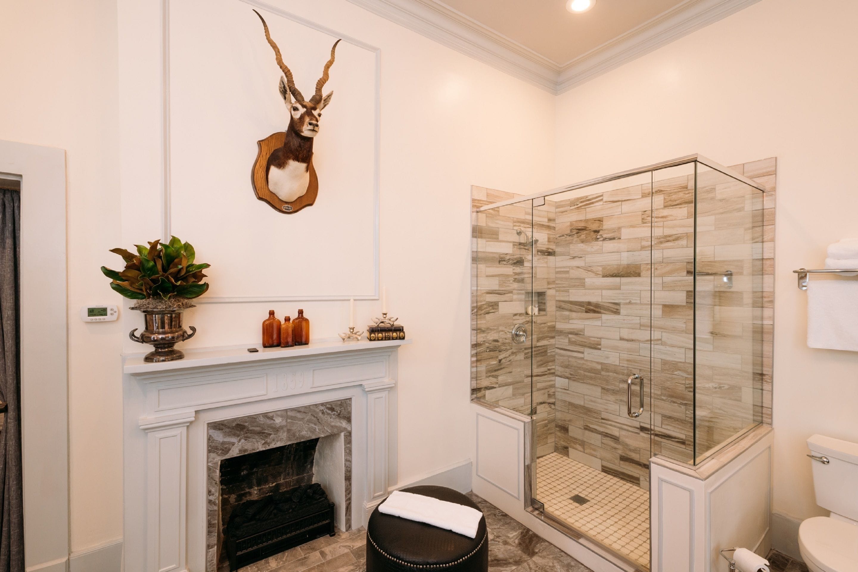 Une salle de bain avec une douche en verre, une cheminée et une tête d’animal fixée au mur.
