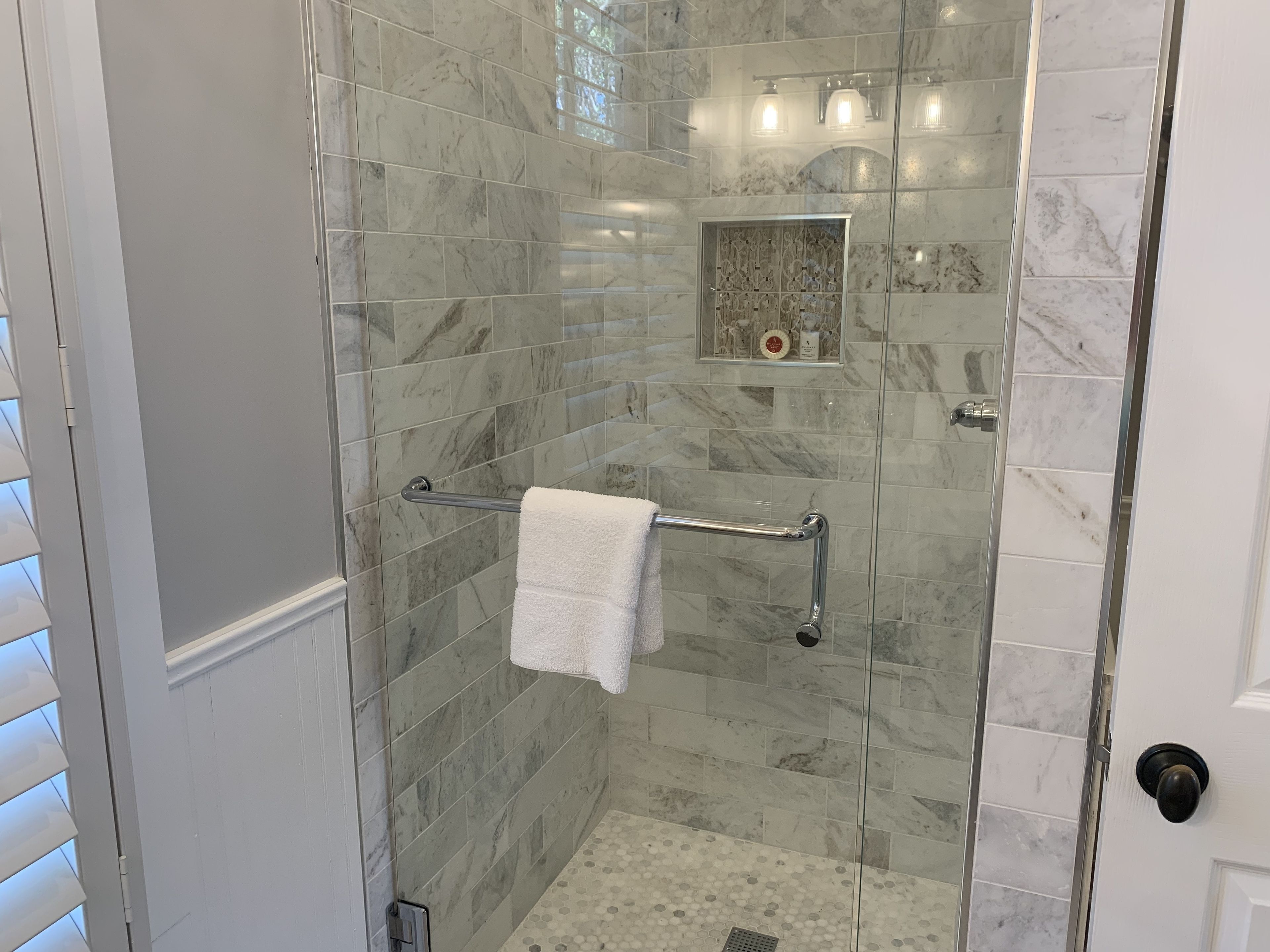 Une douche fermée par des parois de verre, avec une serviette blanche posée sur un porte-serviettes en métal, des carreaux de marbre et un petit objet décoratif accroché au mur.