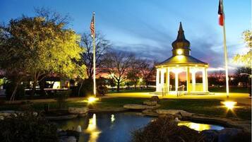 A gazebo with a dome roof and a small pond in front, surrounded by trees and flags.