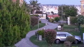 A paved pathway leading to a parked car, surrounded by greenery and buildings in the background. - Exquisite Poolside Apt at the fabulous Oasis Parque. Unlimited WiFi IPTV etc (Portimão)