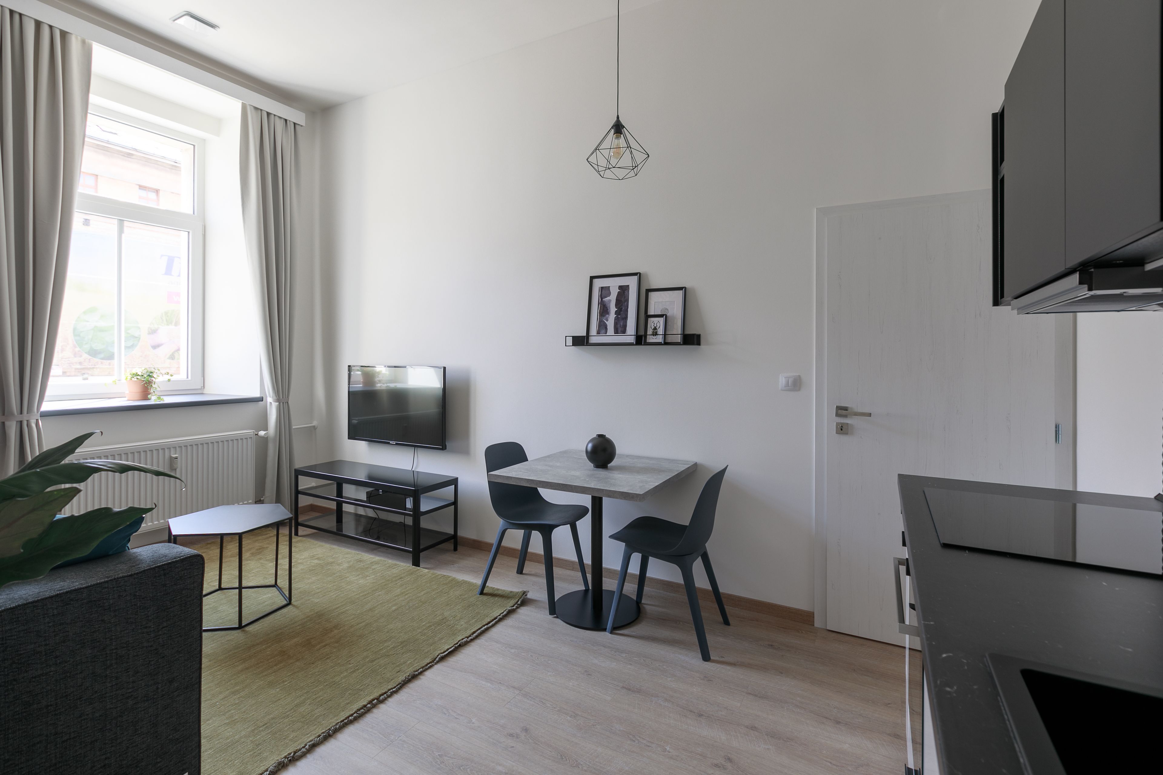 A modern kitchen with a dining area, a TV, and a window with curtains.