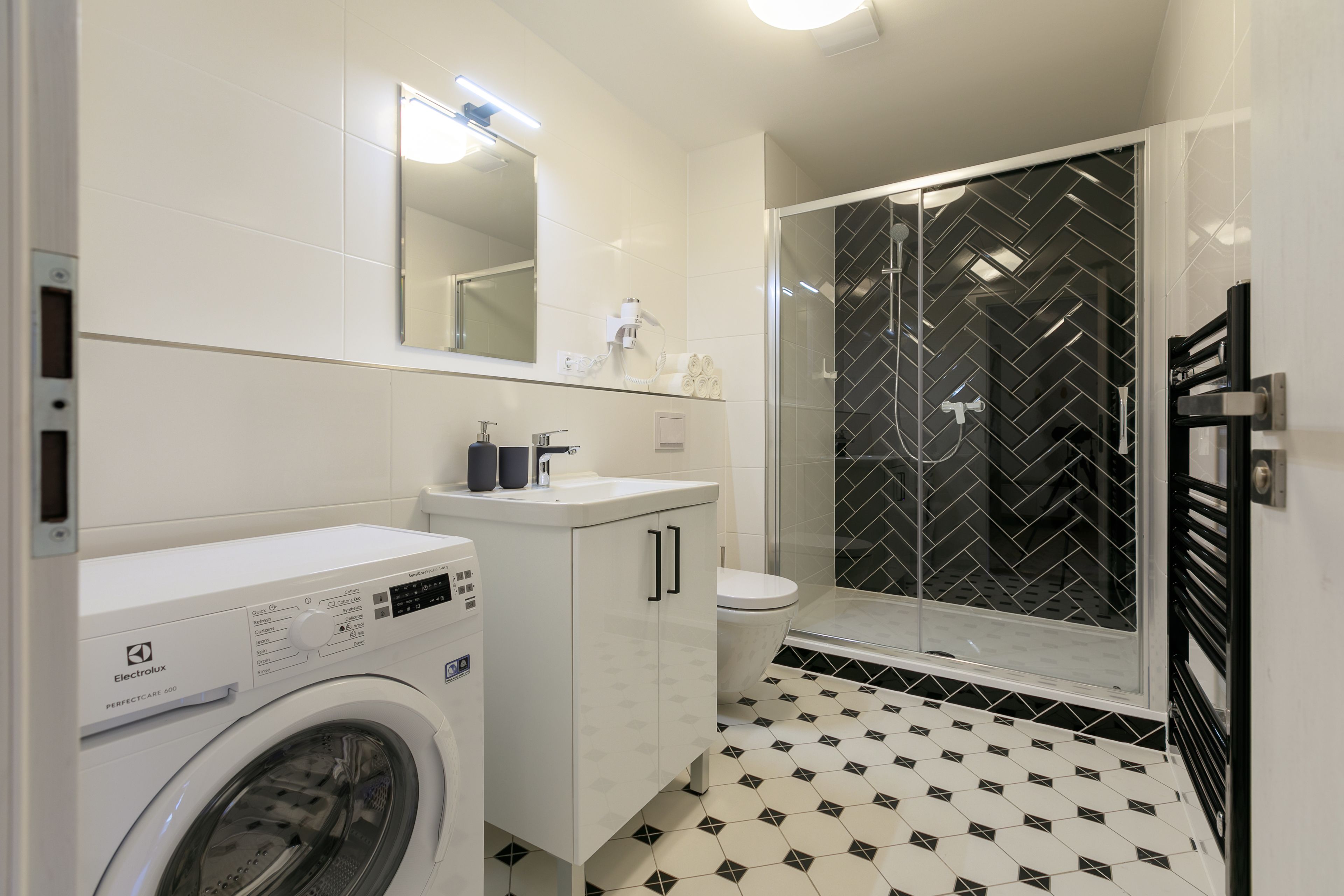 A compact bathroom with a washing machine, a toilet, and a glass-enclosed shower.