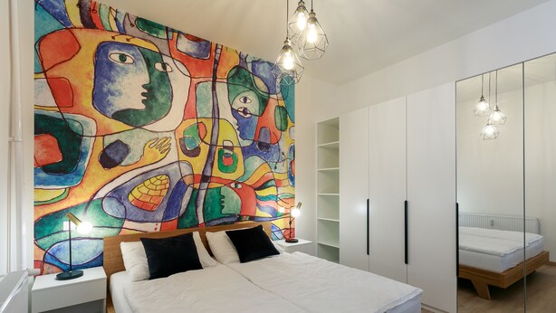 A modern bedroom with a large bed, a colorful abstract painting on the wall, and a wardrobe with a mirror. - Avantgarde apartments (Plzen)