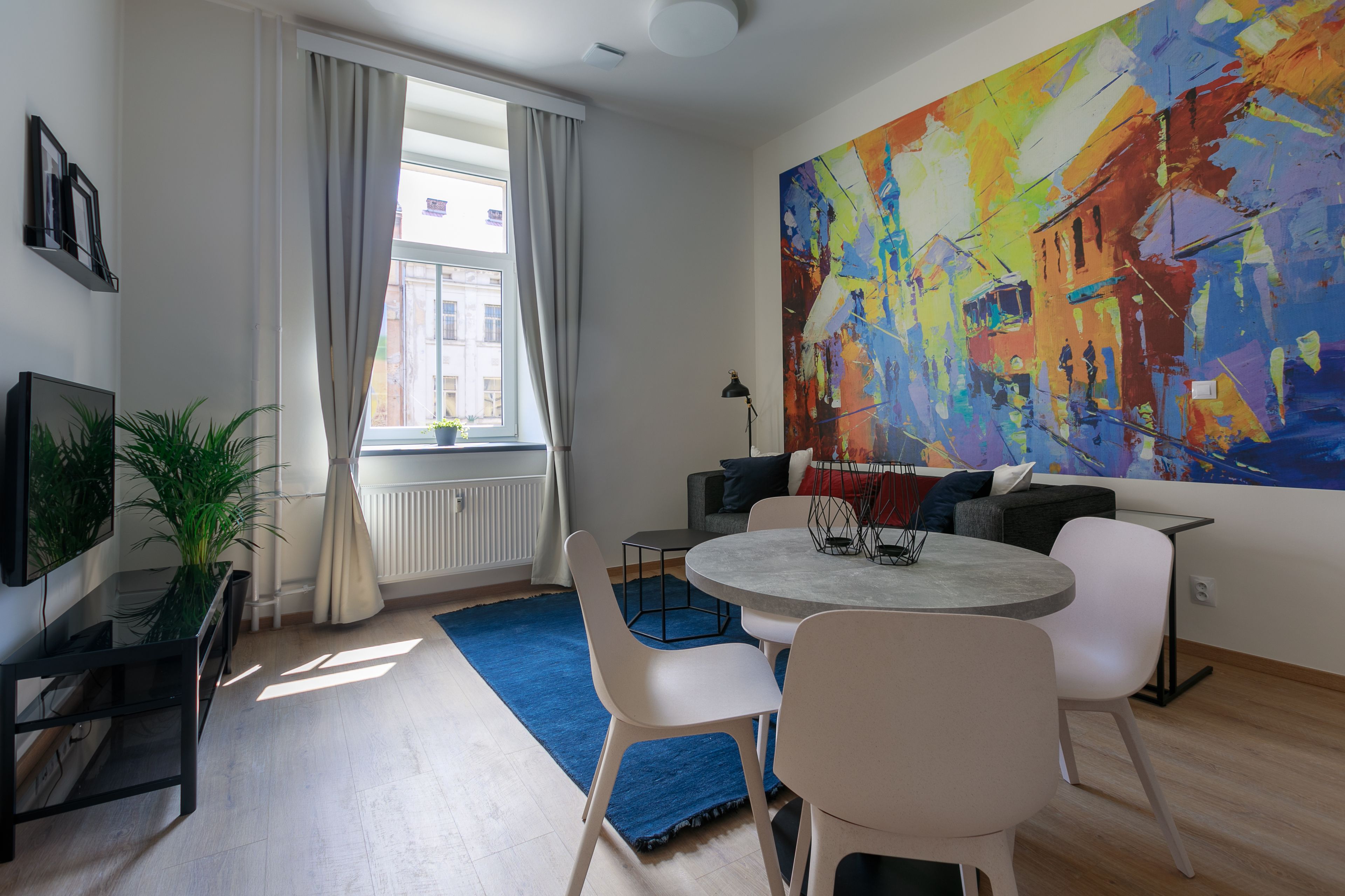 Un salon moderne avec une table de salle à manger ronde, des chaises blanches, un grand tableau abstrait et une vue sur la rue par une fenêtre.