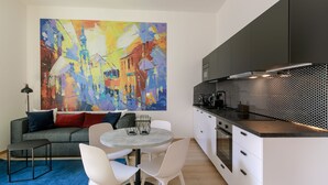 A modern kitchen with a black countertop, white cabinets, and a large abstract painting on the wall. - Avantgarde apartments (Plzen)