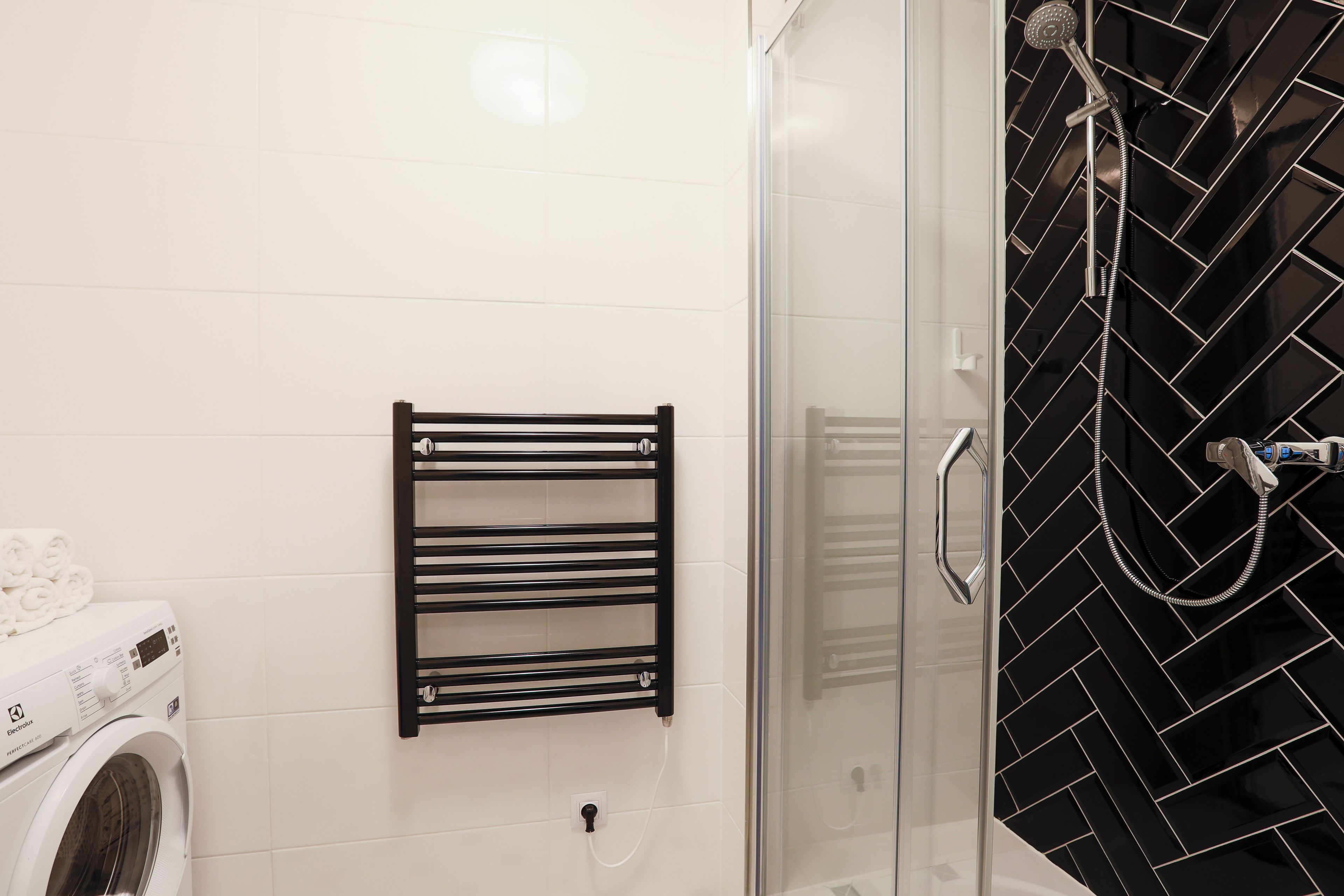 Ein Badezimmer mit Waschmaschine, schwarzem Handtuchhalter und Dusche mit schwarzem Fliesenspiegel.