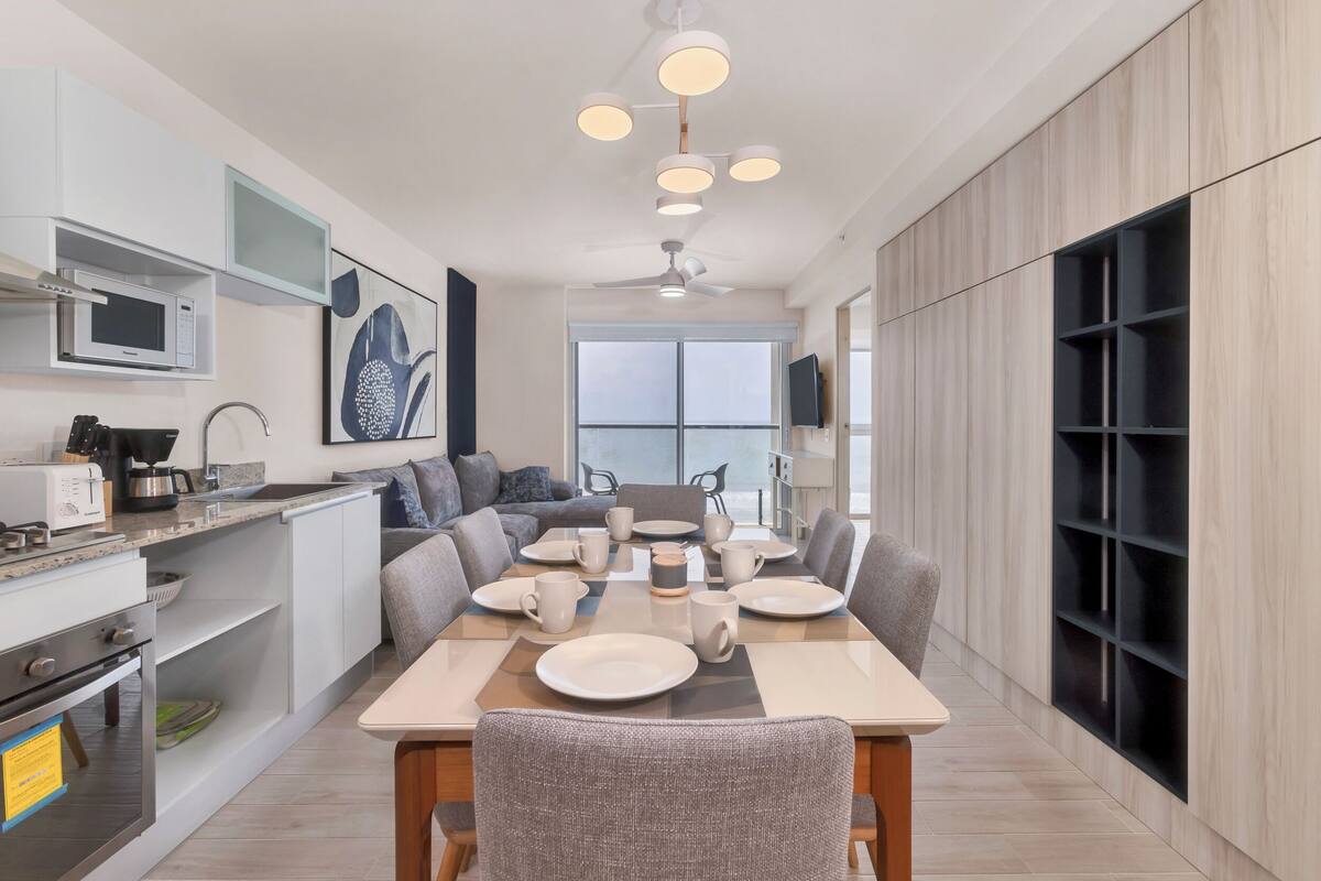 A modern kitchen with a dining area, white cabinetry, a built-in microwave, and a large window.