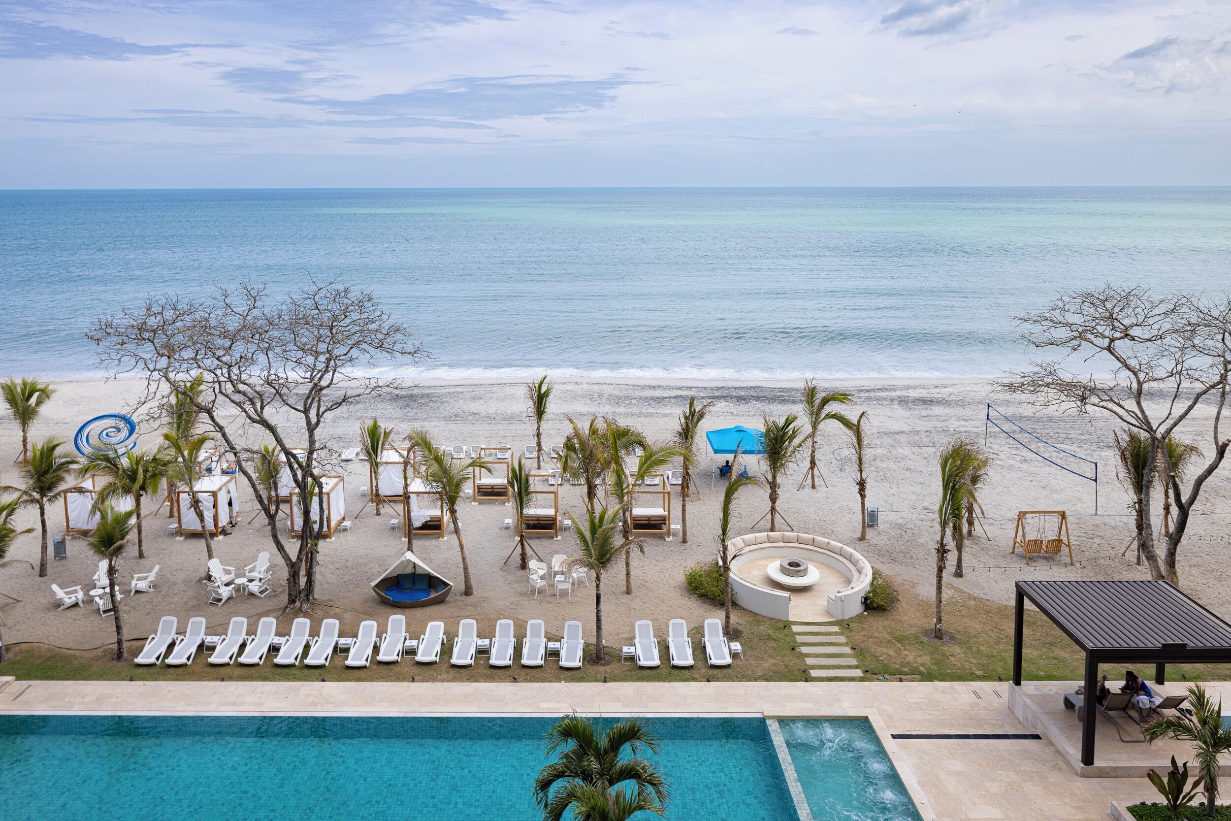 Un resort frente a la playa con piscina, sillones de descanso y una silla colgante.
