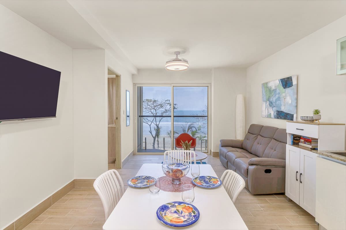 A dining area with a table set for four, a sofa, and a view of the sea through a glass door.