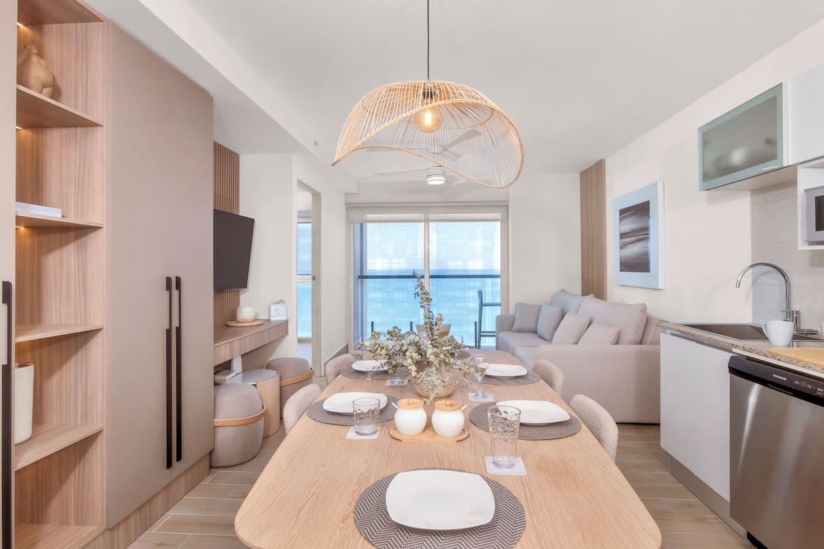 A modern kitchen with a dining area, large windows, and a view of the sea.