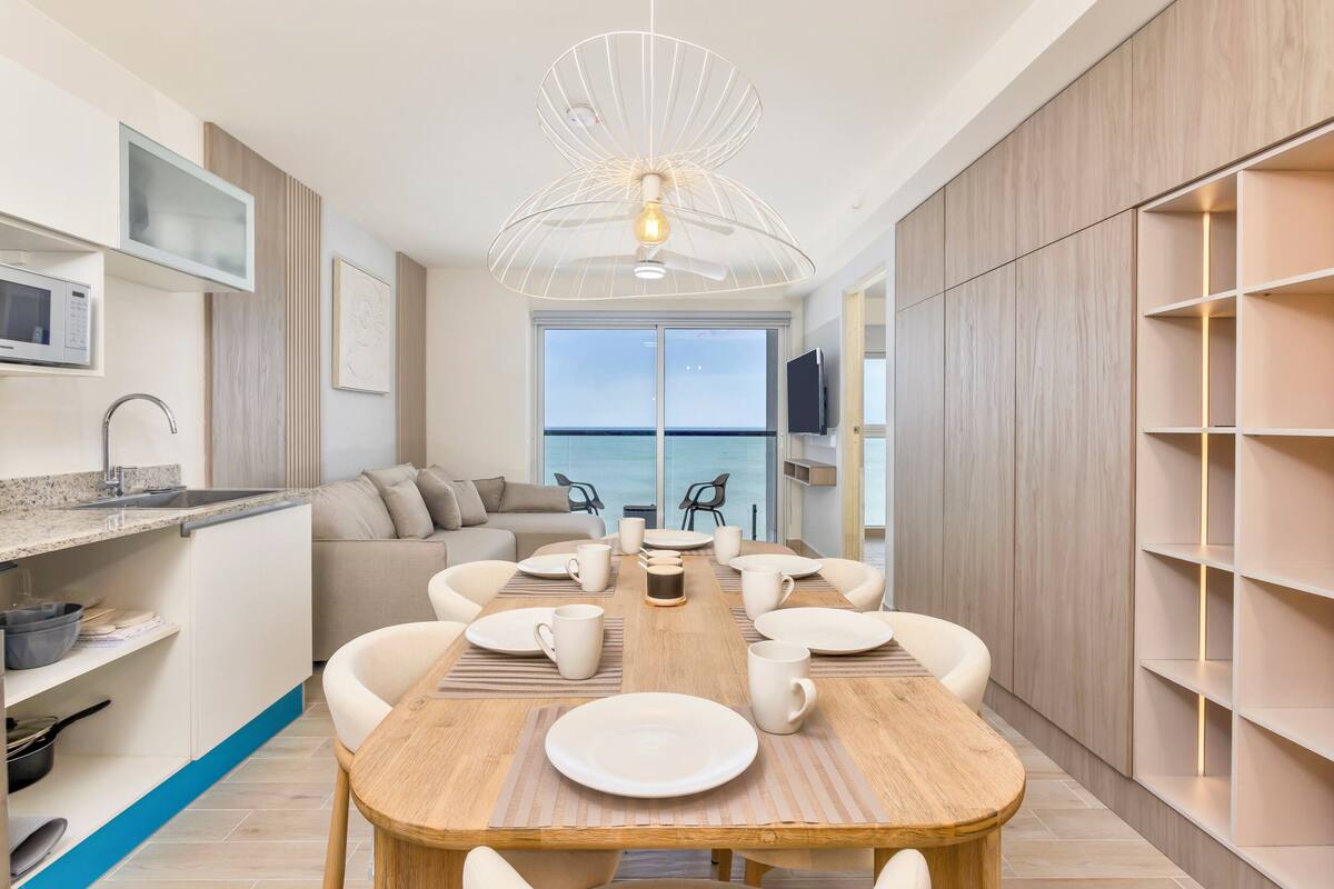 A modern kitchen with a dining area, a large window, and a view of the sea.