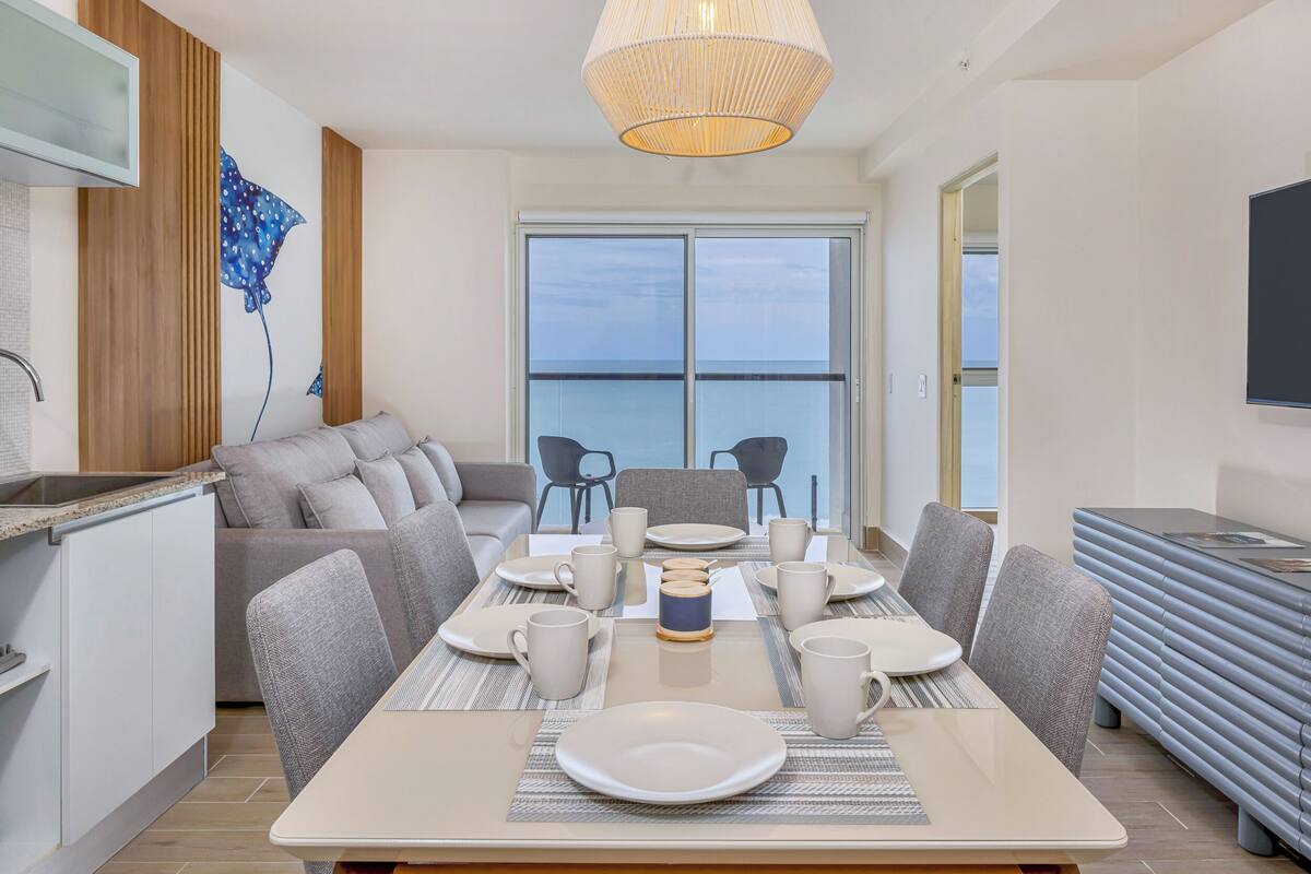 A modern dining area with a large table set for six, a sofa, and a television.