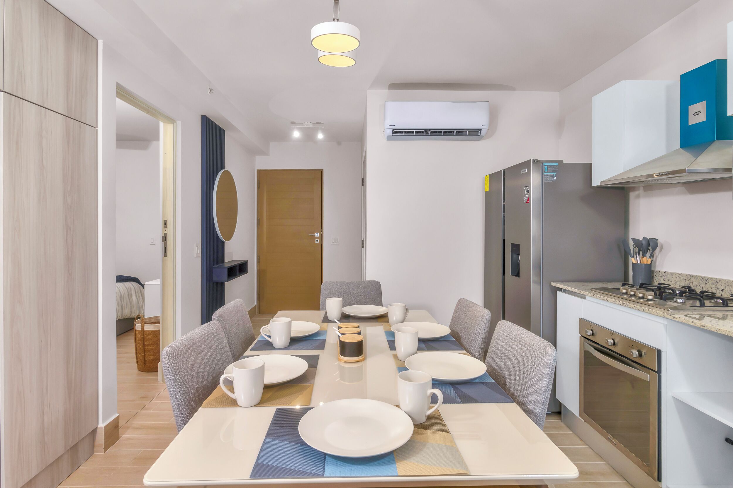 A modern kitchen with a dining area, equipped with a refrigerator, stove, and dining table set for six.