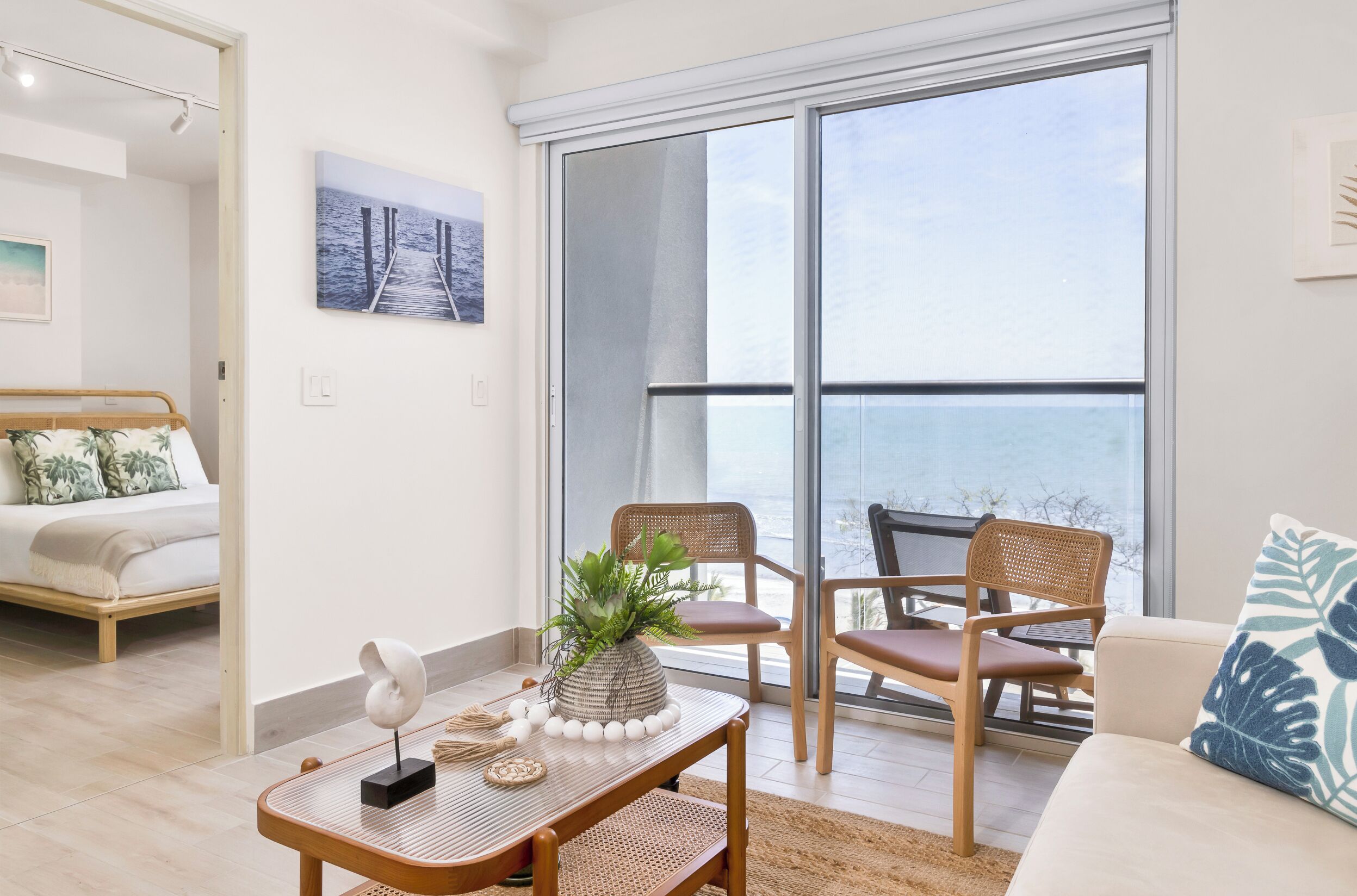 Een moderne woonkamer met een grote schuifdeur naar een balkon, een bed met uitzicht en een salontafel met decoratieve objecten.