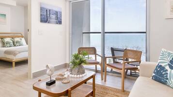 Een moderne woonkamer met een grote schuifdeur naar een balkon, een bed met uitzicht en een salontafel met decoratieve objecten.