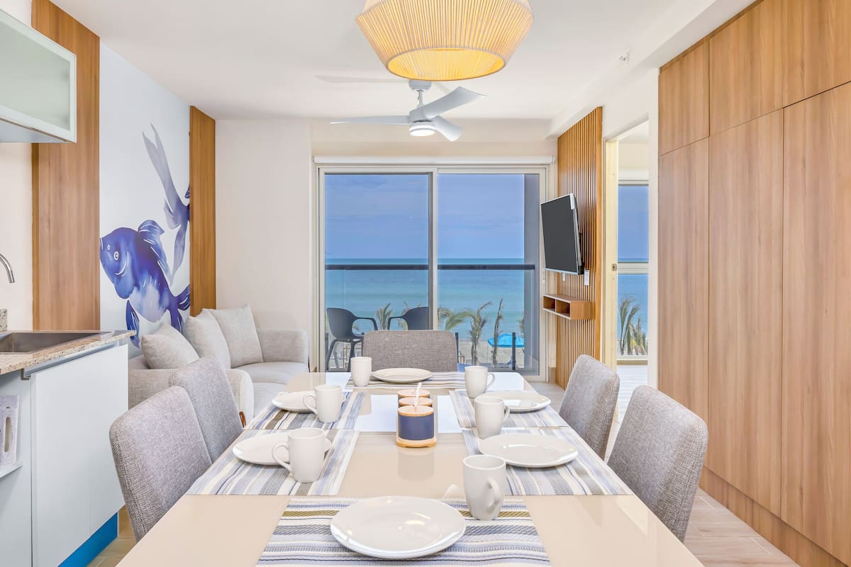 A dining area with a view of the ocean, a ceiling fan, and a TV mounted on the wall.