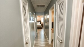 Un couloir doté d’un plancher en bois et de portes blanches, qui mène à une chambre avec un lit et une table de chevet.