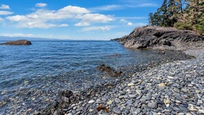 Una costa rocosa con agua cristalina, una isla distante y un acantilado cubierto de bosque.