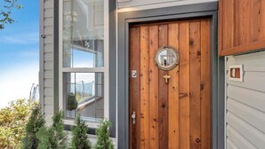 Una puerta de madera con un espejo circular encima, un buzón pequeño y una ventana con vistas al exterior.